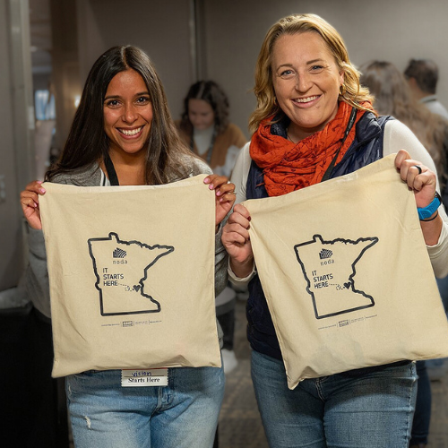 Two volunteers working at check-in and holding welcome bags up. for NODAC 2023. 